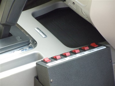 A close-up view of a car's interior showing a console with several red buttons and a compartment with a black rubber mat.